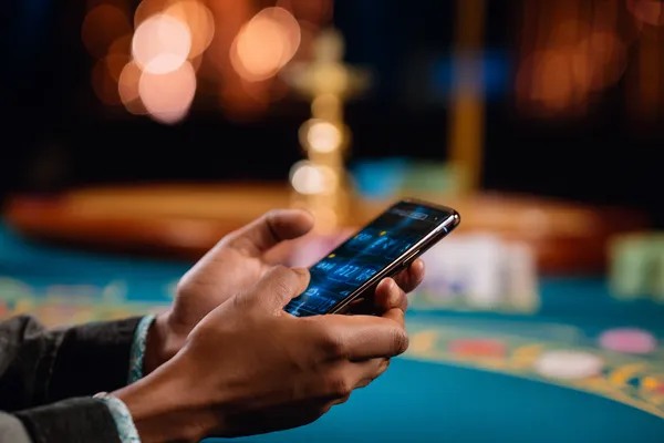 Un joueur utilise son smartphone lors d'un événement festif local, représentant le casino KWANZA entièrement adapté au mobile.